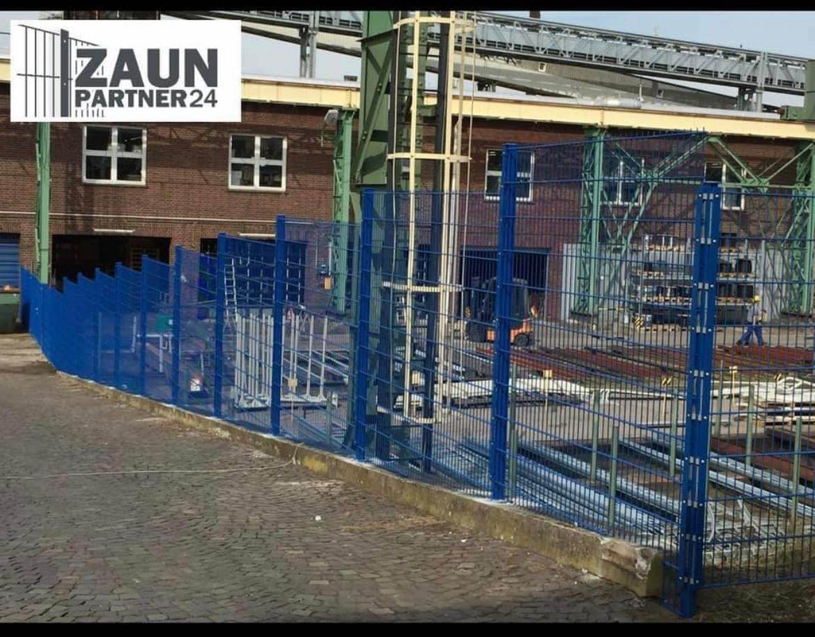 Blau beschichteter Industriezaun aus hohen Gittermatten entlang eines gewerblichen Betriebsgeländes.